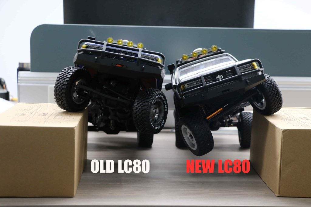 New and old JXC 1:12 LC80 and Land Rover RC crawlers compared and parked on same size cardboard boxes
