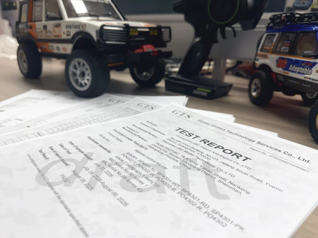RC model cars and a radio controller displayed on a desk, with export and testing documents spread out in the foreground.