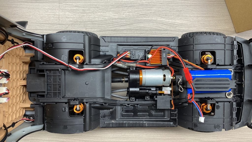 Underside view of an RC car chassis showing the 550 brushed motor, 40A ESC, LiPo battery, and four-wheel drive shaft assembly with metal oil-filled shocks