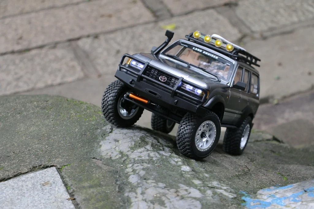 Silver LC80 Land Cruiser RC crawler climbing rocks with articulated front suspension