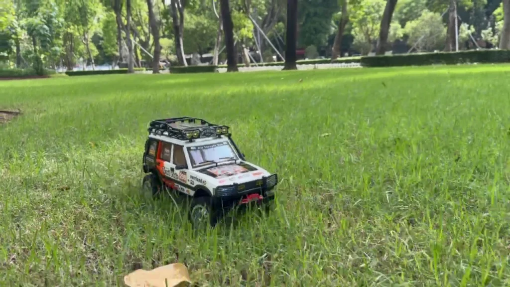 White RC crawler with racing livery driving across park grass