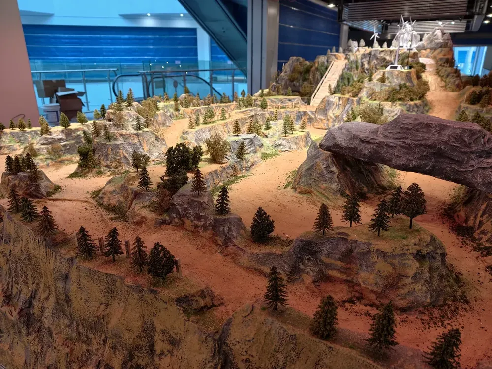 Close-up of a finished indoor RC diorama track installed in a shopping mall, showing sealed desert terrain and rock detail - JXC Model